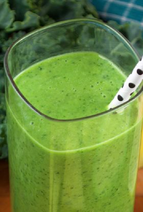 Green smoothie in a glass with a white paper straw that has black polka dots.