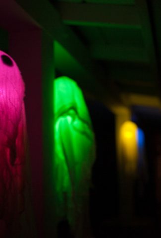 Floating ghosts glowing in different colors hanging on a porch in the dark.