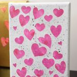 Pink hearts on white canvas with black flecks of paint.
