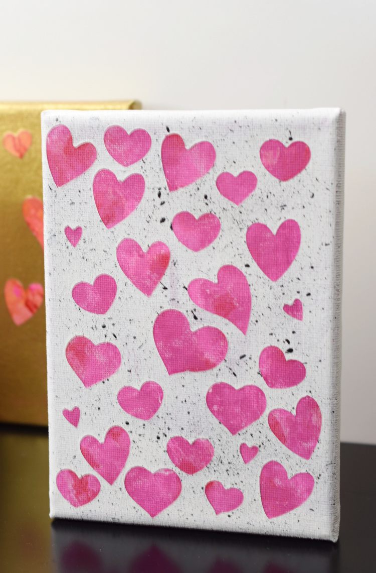 Pink hearts on white canvas with black flecks of paint.