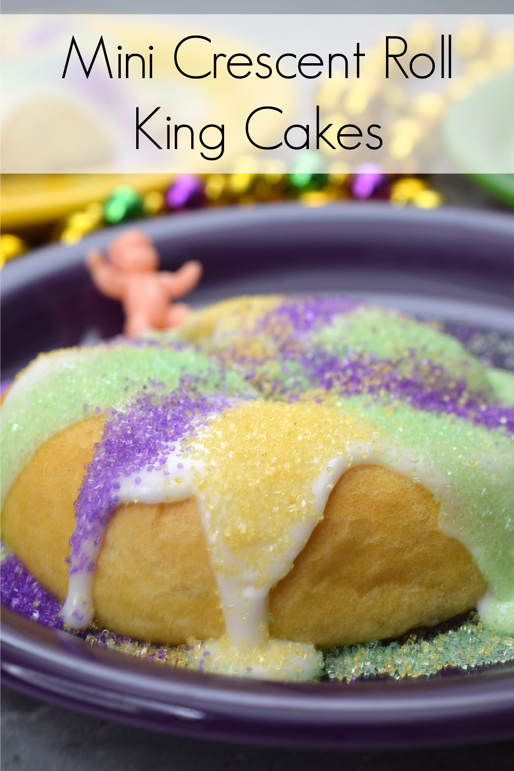 Mini crescent roll king cakes on purple plate with mardi gras beads and plastic baby in the background.