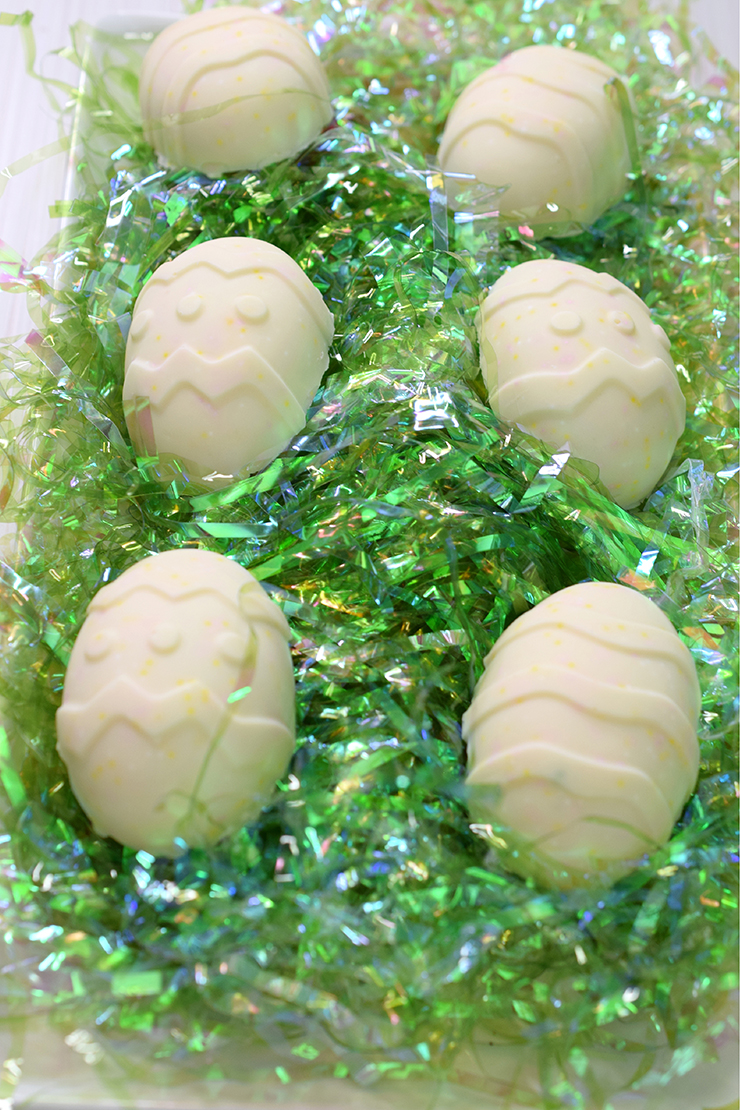Two rows of chocolate pinata Easter eggs on shiny, green Easter grass.