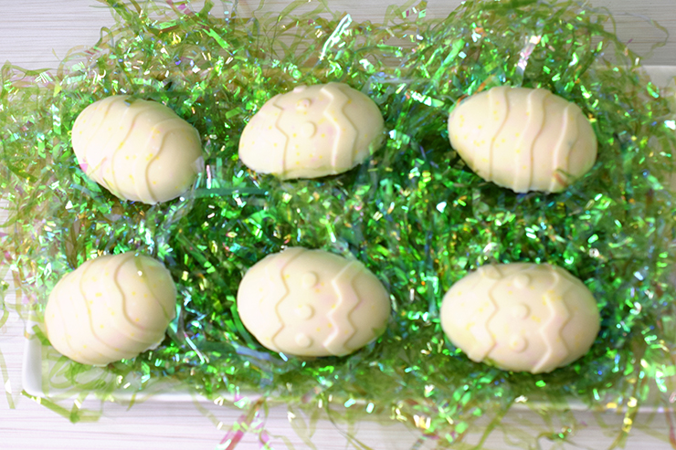 Chocolate Easter eggs sitting on a white platter with shiny green Easter grass.