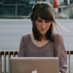Woman sitting at a table working on a laptop, doing a social media audit, with words that read How to audit your own blog and social media profiles.