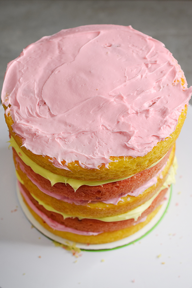 Layered cake with lemonade and strawberry cake layers alternating and pink and yellow icing alternating.