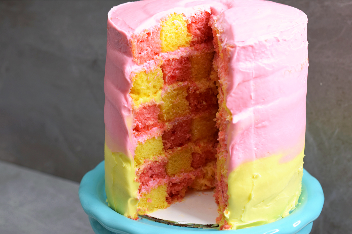 Pink and yellow checkerboard cake on a teal plate.
