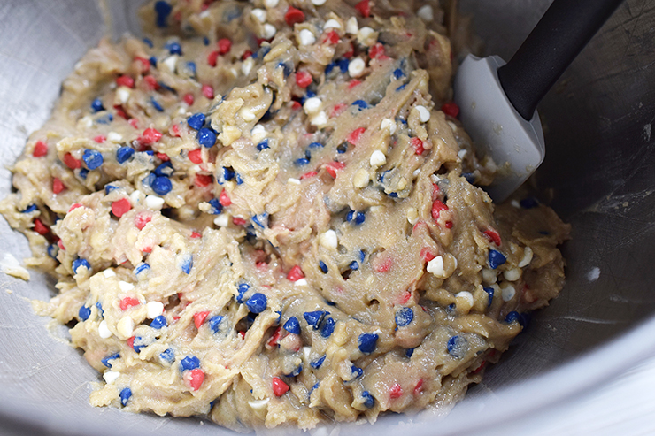 Cookie dough with red, white, and blue baking chips being stirred by a spatula.