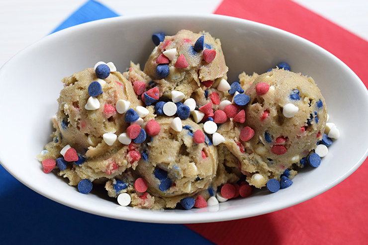 Scoops of unbaked cookie dough with red, white, and blue chips in a white bowl.