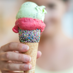 Hand holding an ice cream cone with three different scoops of ice cream under the words Over A Dozen Delicious ice Cream Recipes.