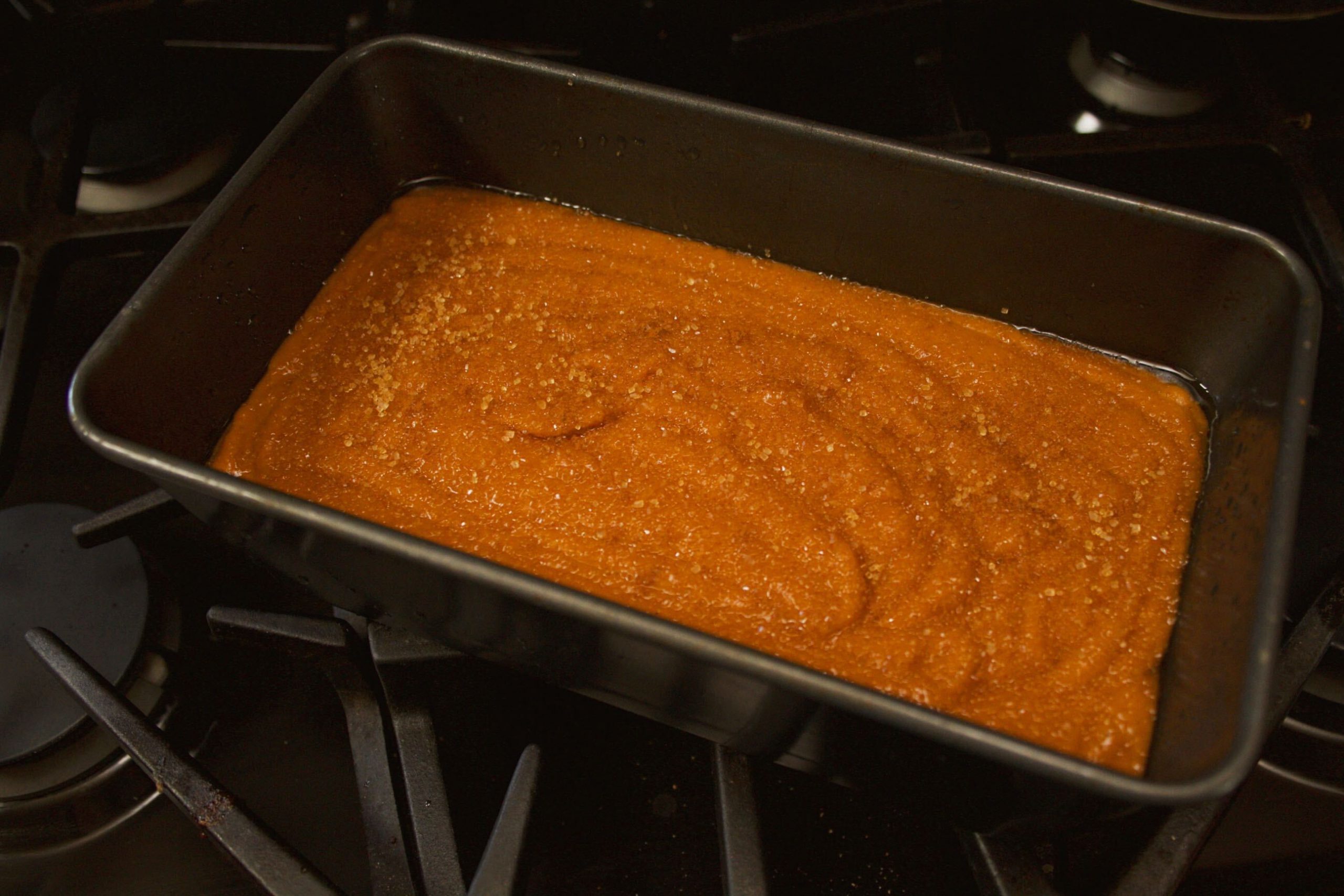 Batter for pumpkin bread in a loaf pan sitting on an oven.