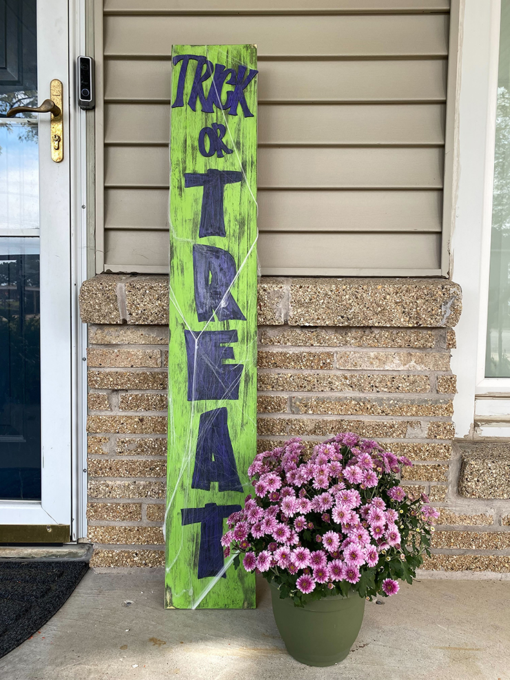 Spooky green trick or treat sign with purple lettering and fake spiderwebs. 