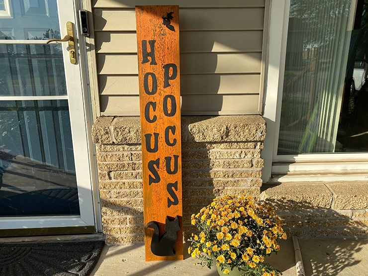 Front porch with a tall sign by the door that reads Hocus Pocus and has a silhouette of a witch riding on a broom.