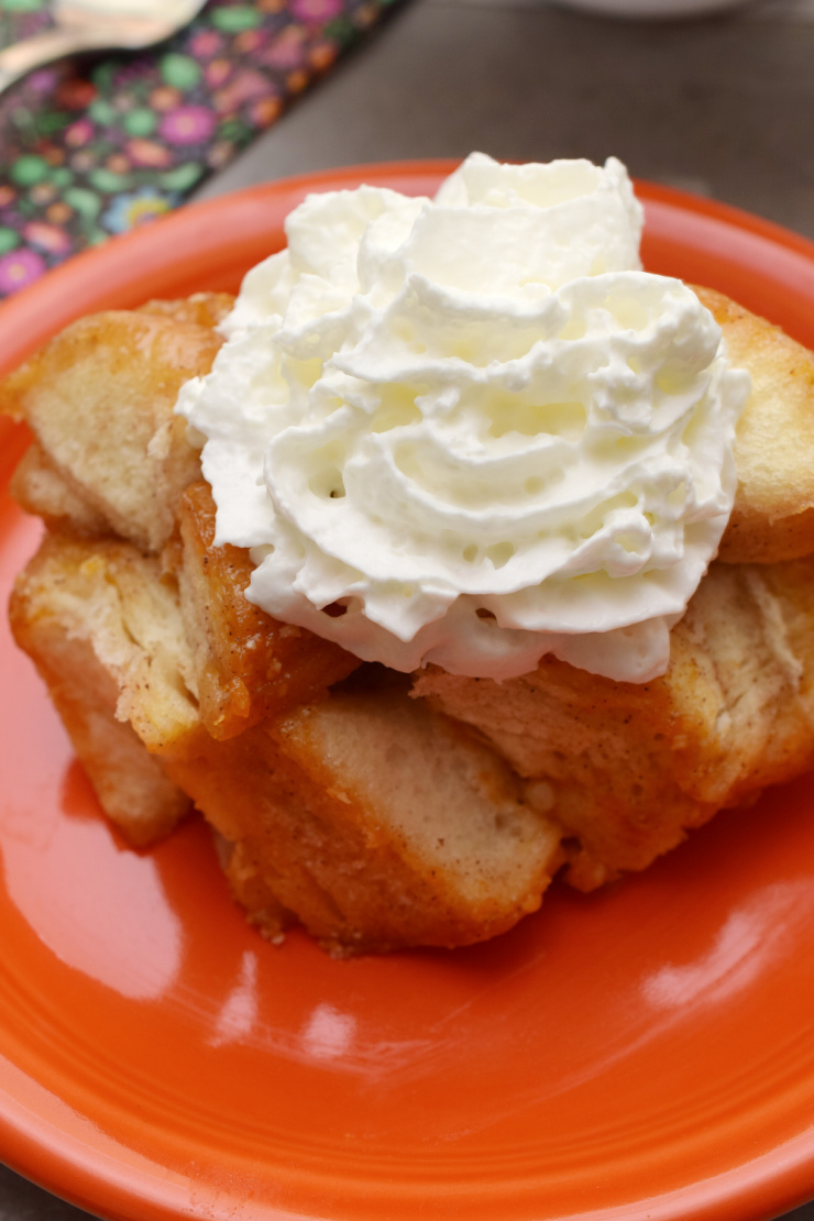 Orange plate with a serving of pumpkin spice monkey bread with whipped cream on top.