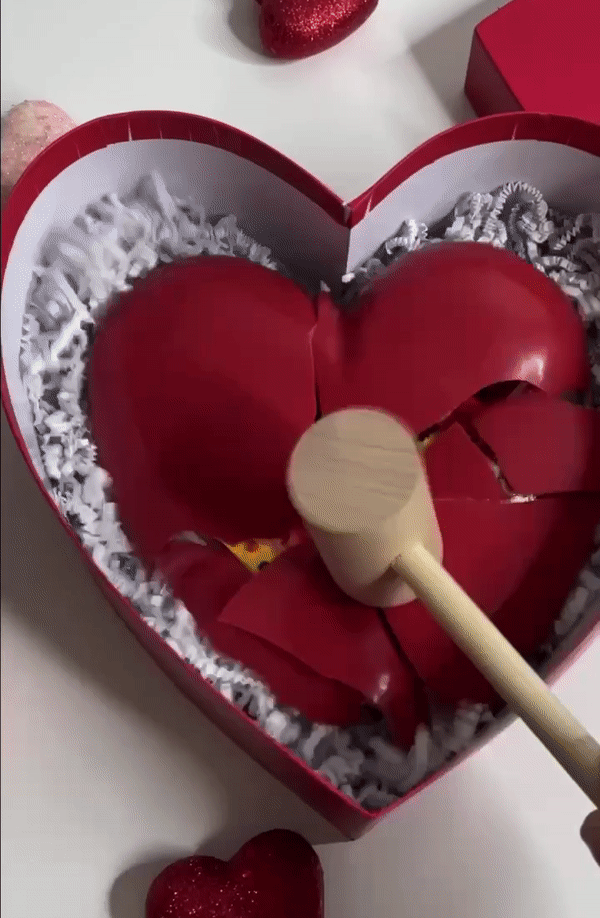 Wooden mallet breaking a red, chocolate heart pinata to reveal the candy below. 