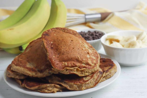 Stack of peanut butter pancakes sitting in front of bananas and chocolate chips.
