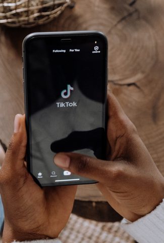 Black woman holding a phone with the TikTok app showing.