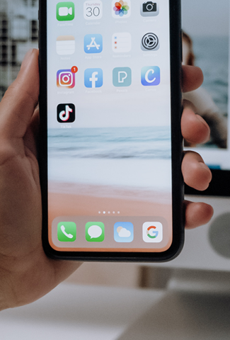 Hand holding a phone with icons showing, including the TikTok app icon.