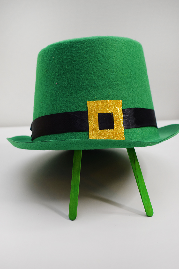 Green, felt hat being held up with popsicle sticks that have been painted green.