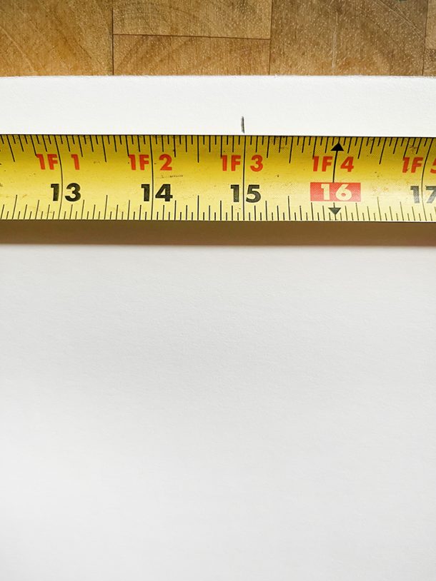 Measuring tape on top of a piece of foam board with a mark at the center point of the board.
