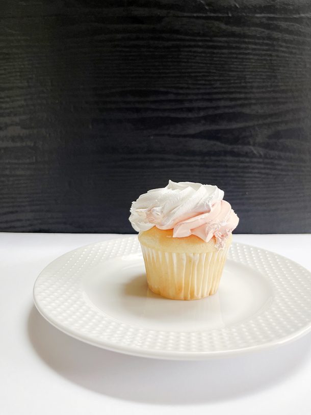 Cupcake on a white plate in front of a black photography background.
