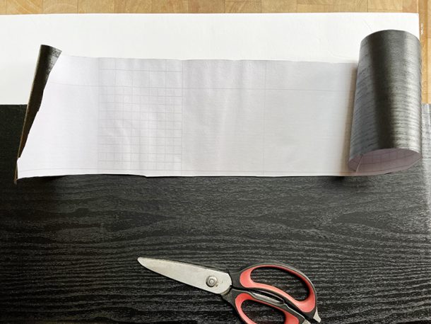 Black, wood-grain contact paper and pair of scissors on top of a foam board.