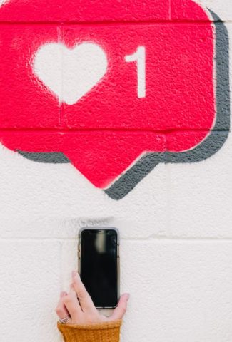 Painting of a like notification in a bubble with a hand holding a phone under it.