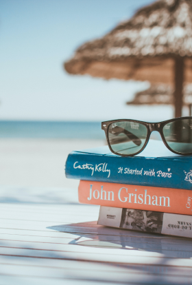 Stack of books with sunglasses on top and the beach in the background.