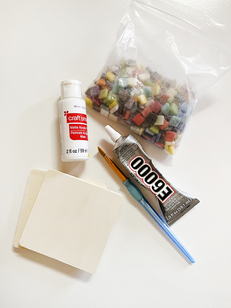 Supplies to make mosaic coasters - mosaic tiles, wooden coasters, grout, glue, mod podge, and paint brush.