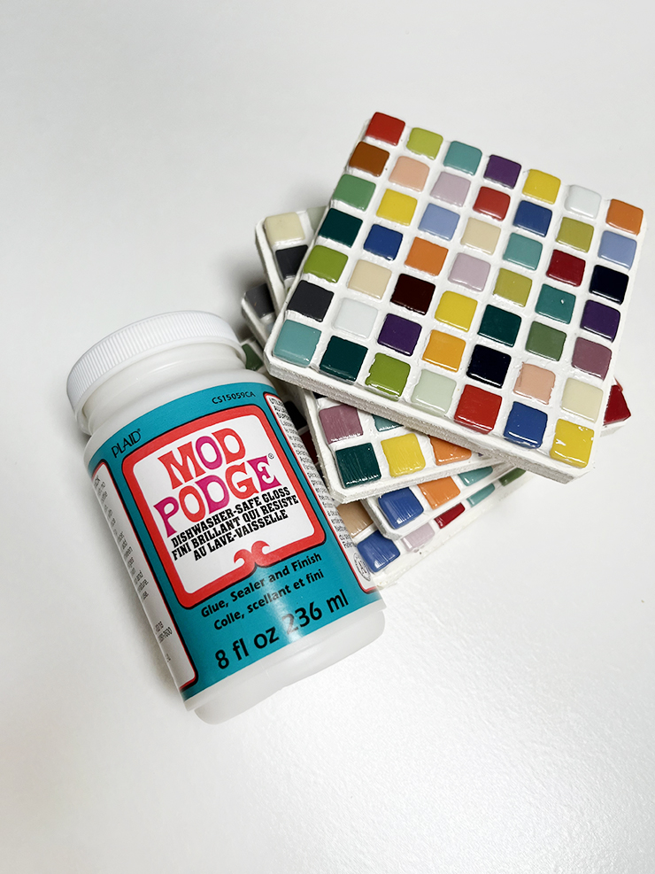Unfinished tile coasters stacked beside a jar of mod podge.