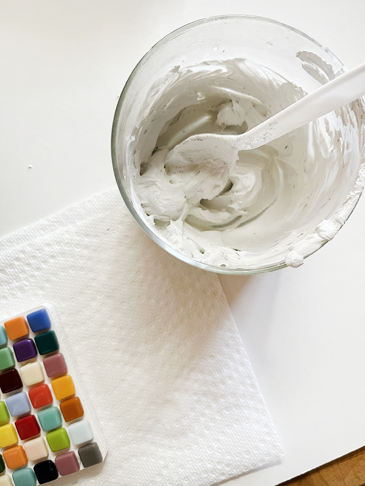 Plastic cup with grout mixture sitting next to coaster on paper towel.