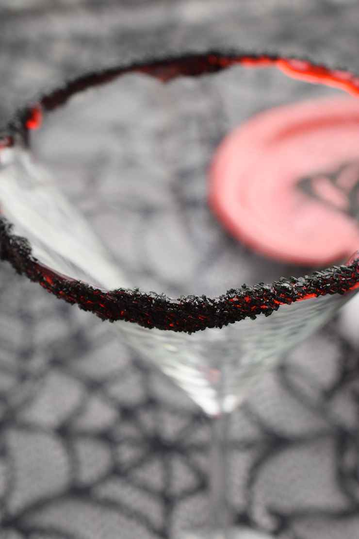 Rim of martini glass with black sprinkles sticking to red gel on the rim.