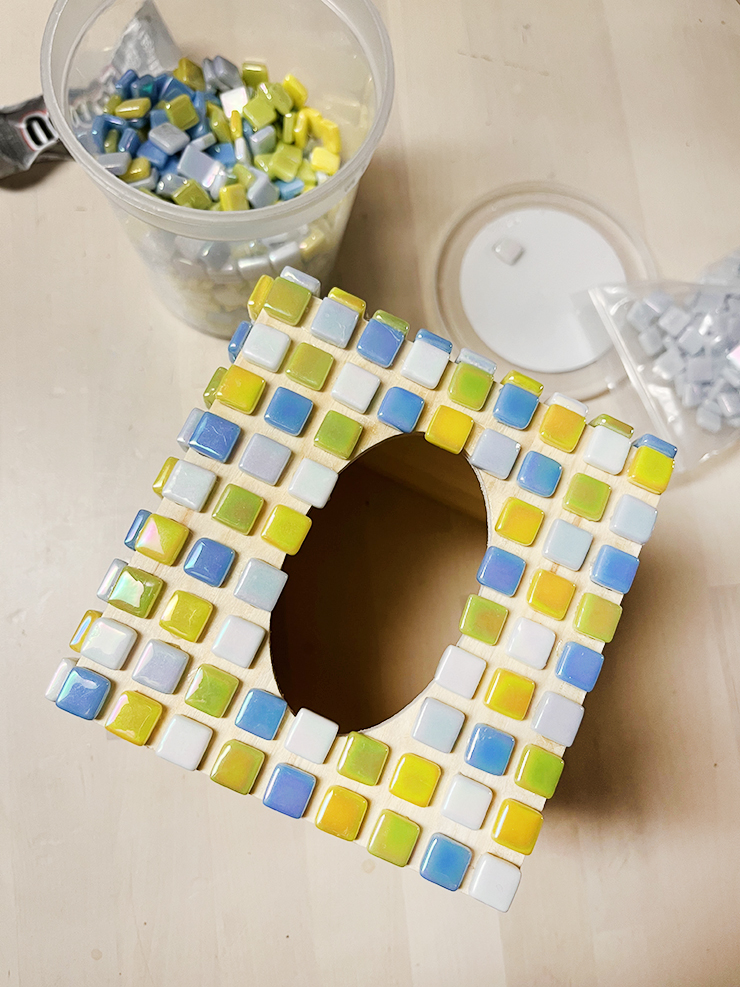 Top view of the tissue box with tiles placed on it. SOme of the tiles are hanging over the edges of the center hole. 