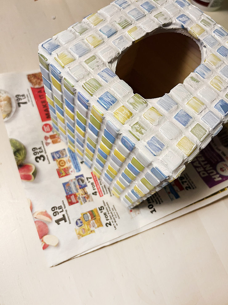 Top view of the tissue box with tiles spread out on it and grout covering the tiles. 