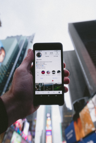 Hand holding phone up in the city with an Instagram profile showing.