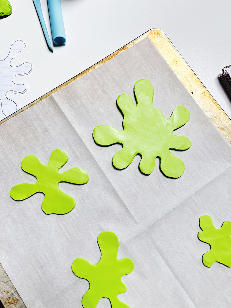 A baking sheet with parchment paper and four green splats of bright green polymer clay.