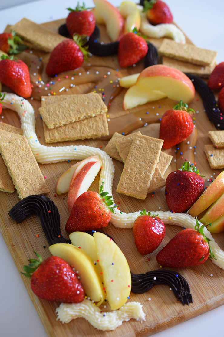 Dessert board with a trio of dips, fruits, and graham crackers.