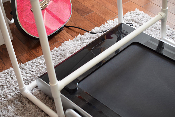 Slim treadmill sitting under a standing desk made with PVC pipes.