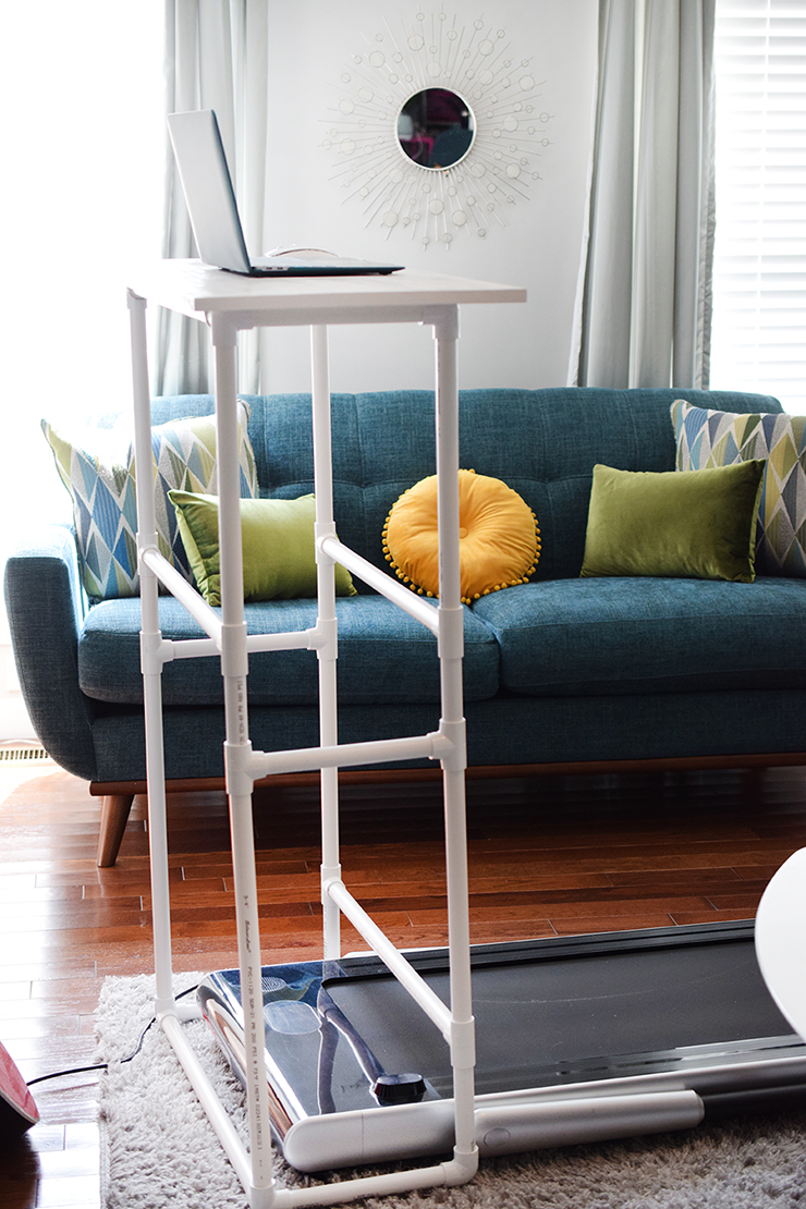 DIY PVC pipe standing desk in a living room with a treadmill under it.