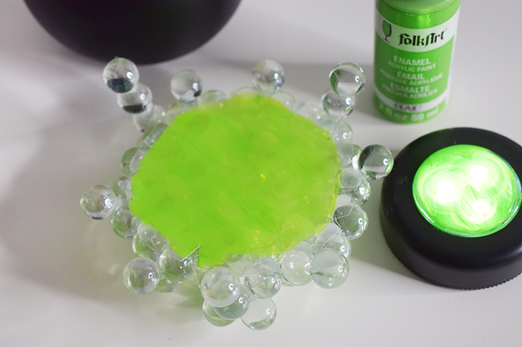 The plastic circle cut from the plate with the marbles glued on top is sitting upside down with bright green pain on the bottom.