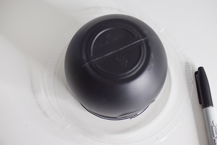 Black plastic cauldron sitting upside down on top of a clear, plastic plate next to a permanent marker.