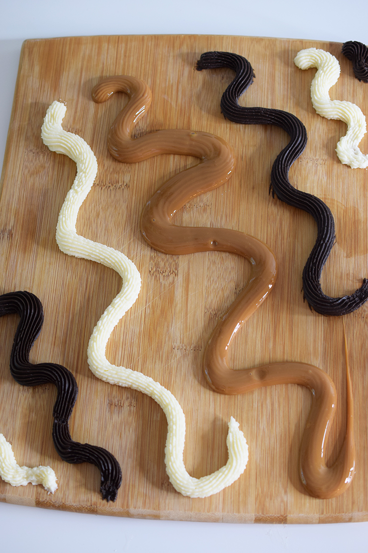 Wooden cutting board with chocolate, vanilla, and dulce de leche dessert dips piped on in squiggly lines.