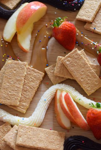 Three dip dessert board with fruit, cookies, crackers, buttercream, chocolate, and dulce de leche.