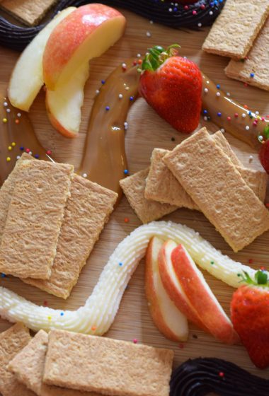 Three dip dessert board with fruit, cookies, crackers, buttercream, chocolate, and dulce de leche.