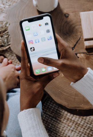 Hands holding a cell phone with social media app icons.